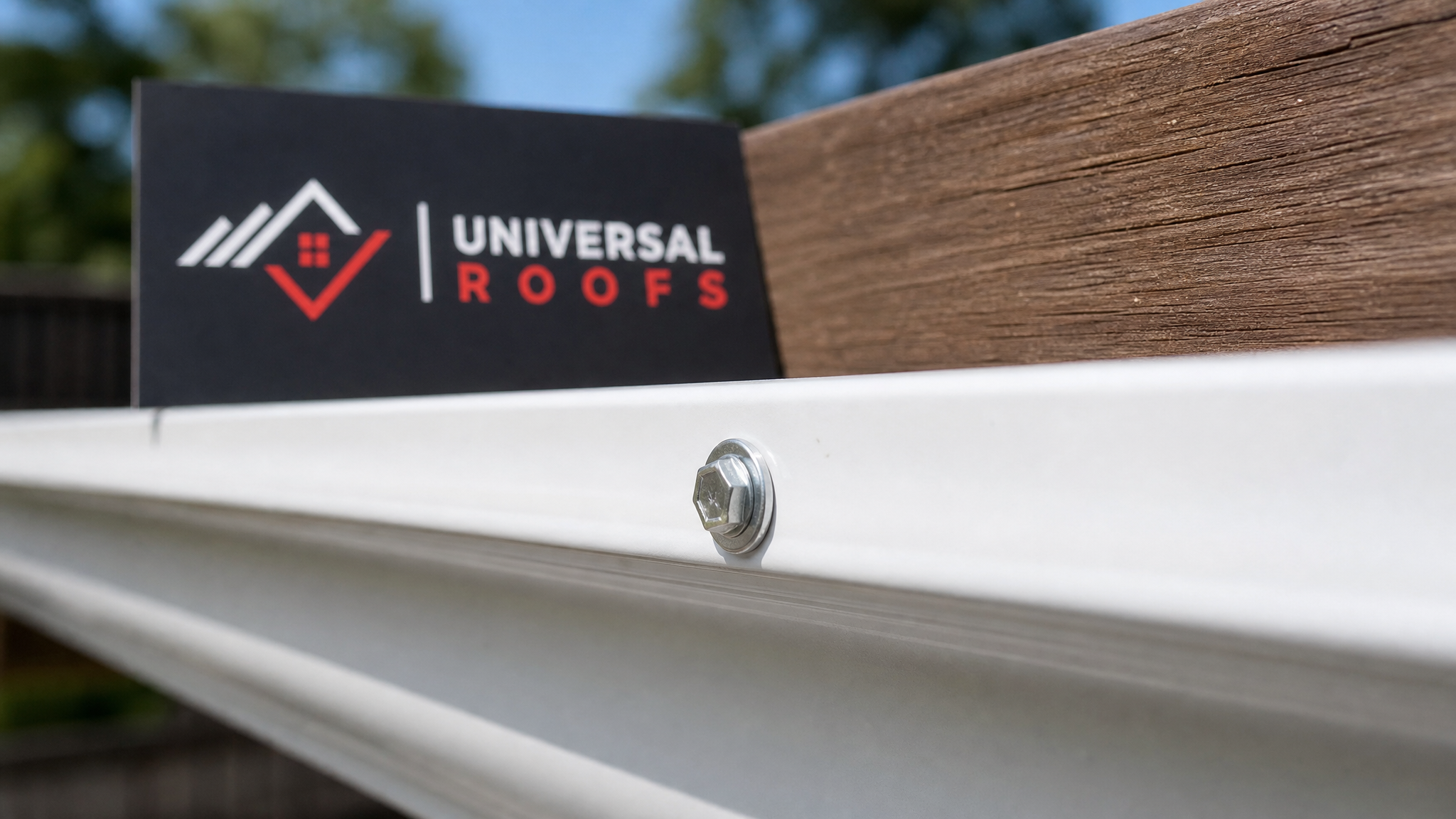Close-up of a hex-head gutter screw seated through a ferrule in an aluminium eavestrough with a small Universal Roofs placard nearby