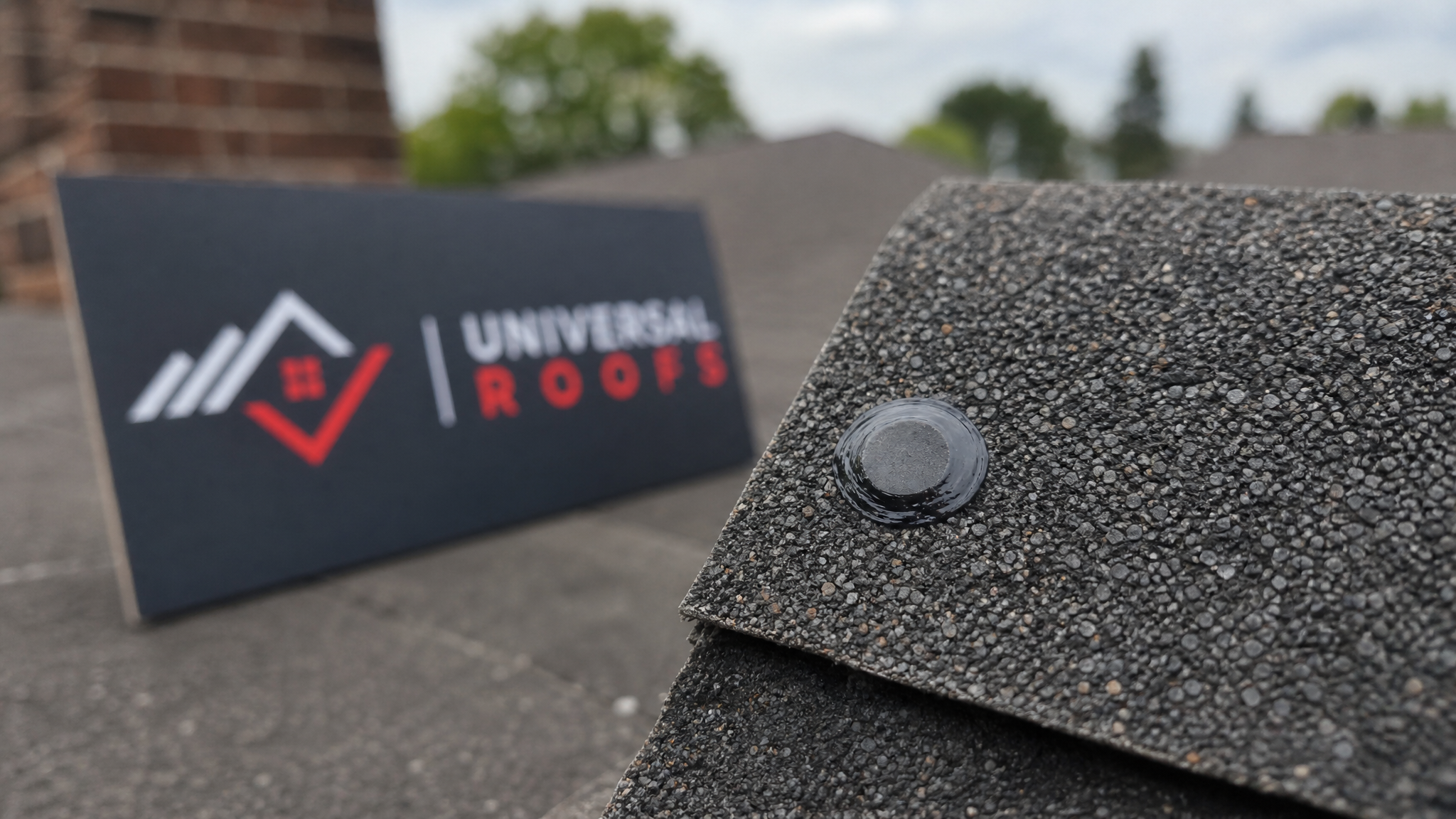 Close-up detail of a properly sealed asphalt shingle nail head with tooled roofing cement bead in daylight