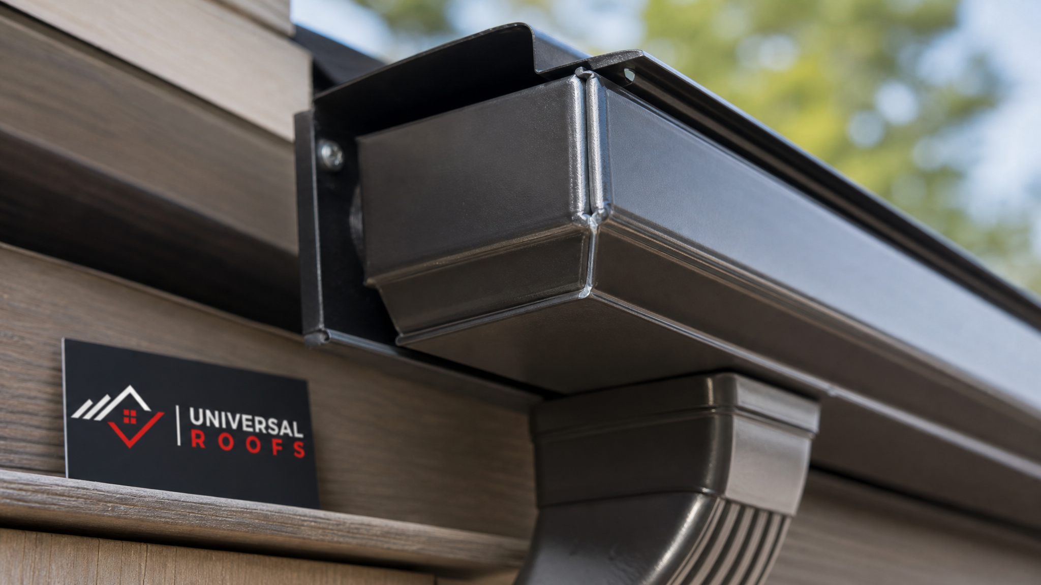 Close-up of a seamless aluminum gutter corner joint and downspout outlet showing correct sealant application and hanger placement
