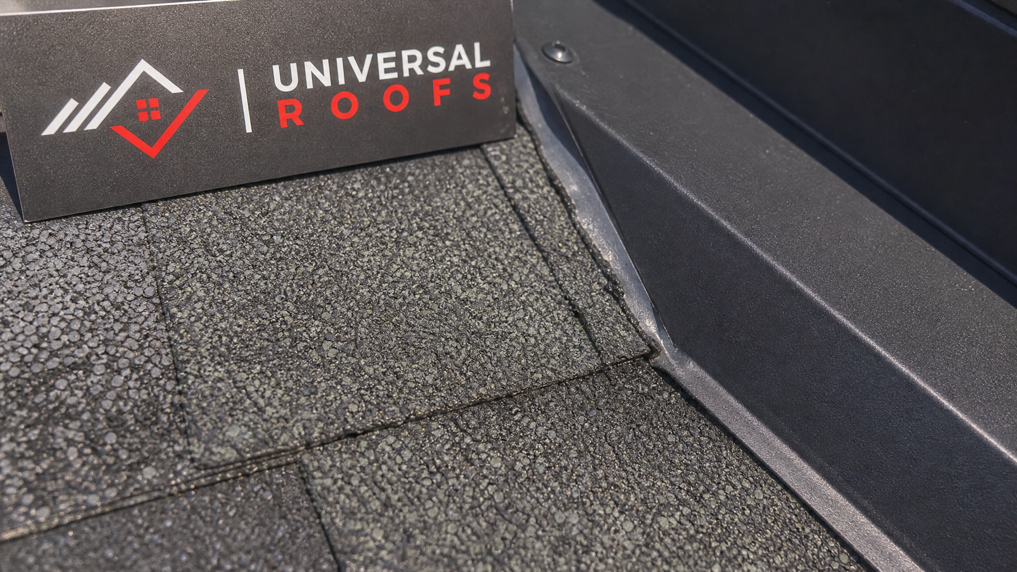 Close-up detail of algae-resistant architectural shingle granules and flashing seam on a Toronto roof with a Universal Roofs branded sign placard visible