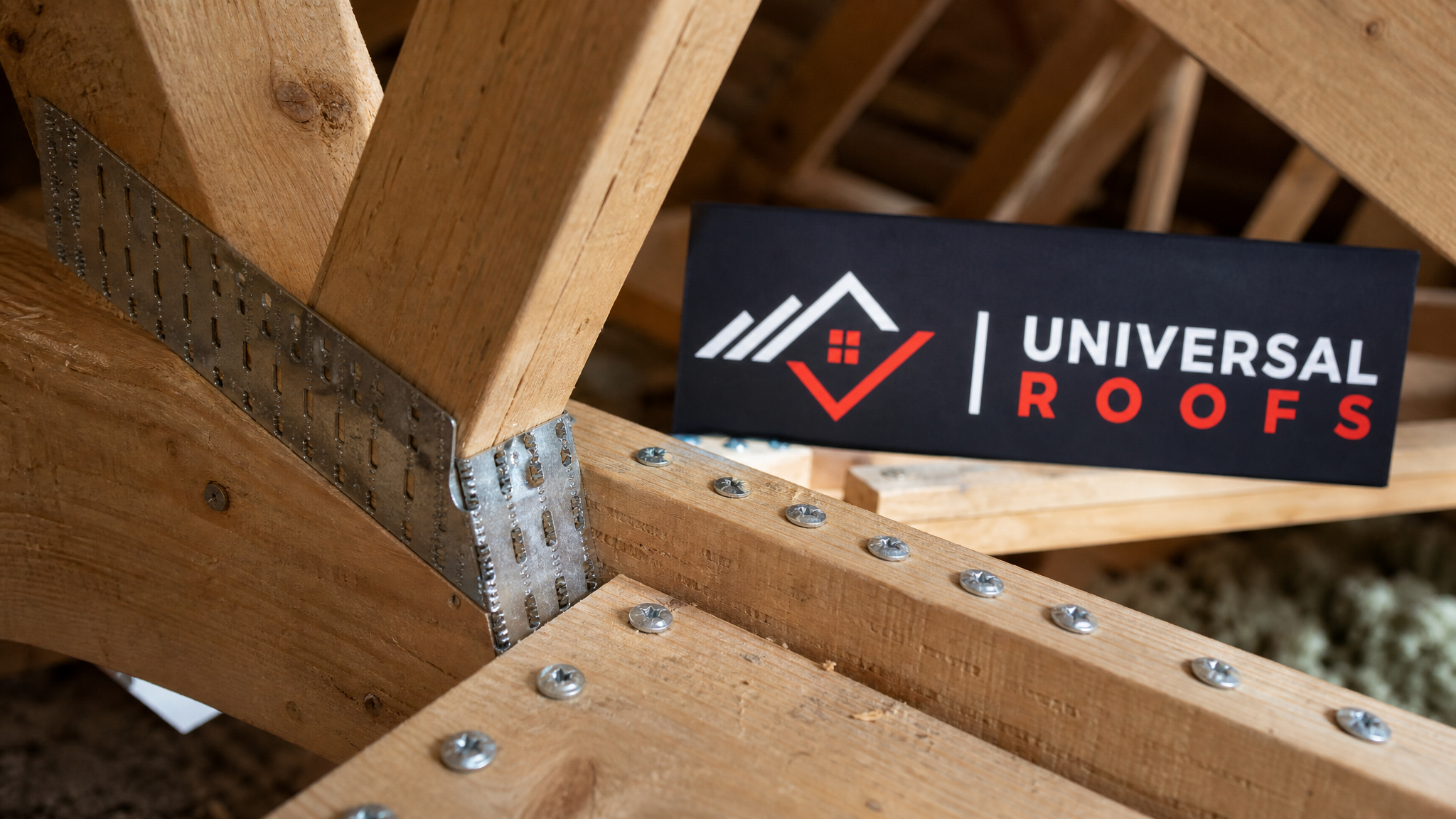 Close-up detail of a metal gusset plate and structural screws reinforcing a wood truss joint with a Universal Roofs branded sign placard nearby