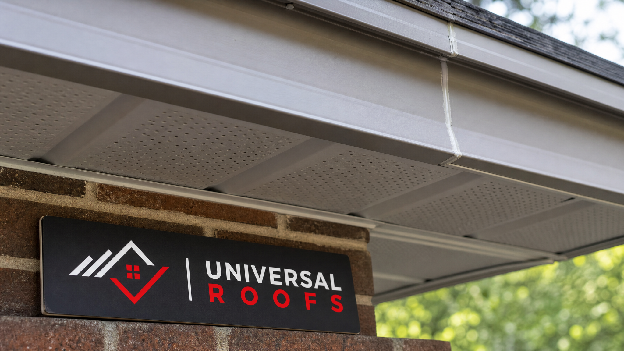 Close-up of vented aluminum soffit panel and fascia joint with fresh caulking, Universal Roofs sign placard beside the roof edge