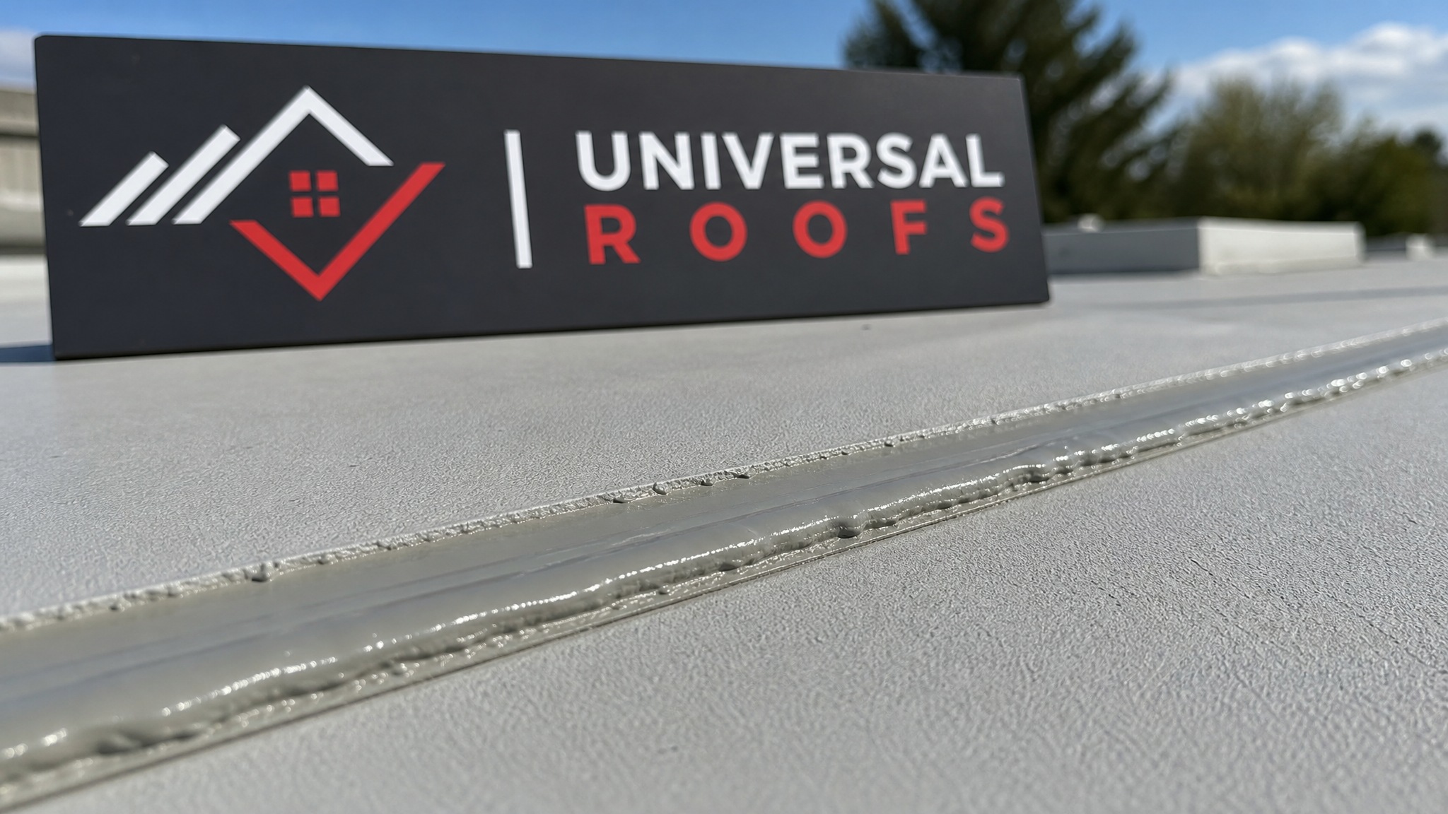 Close-up of cured silicone roof sealant along a commercial membrane seam with a branded sign placard nearby