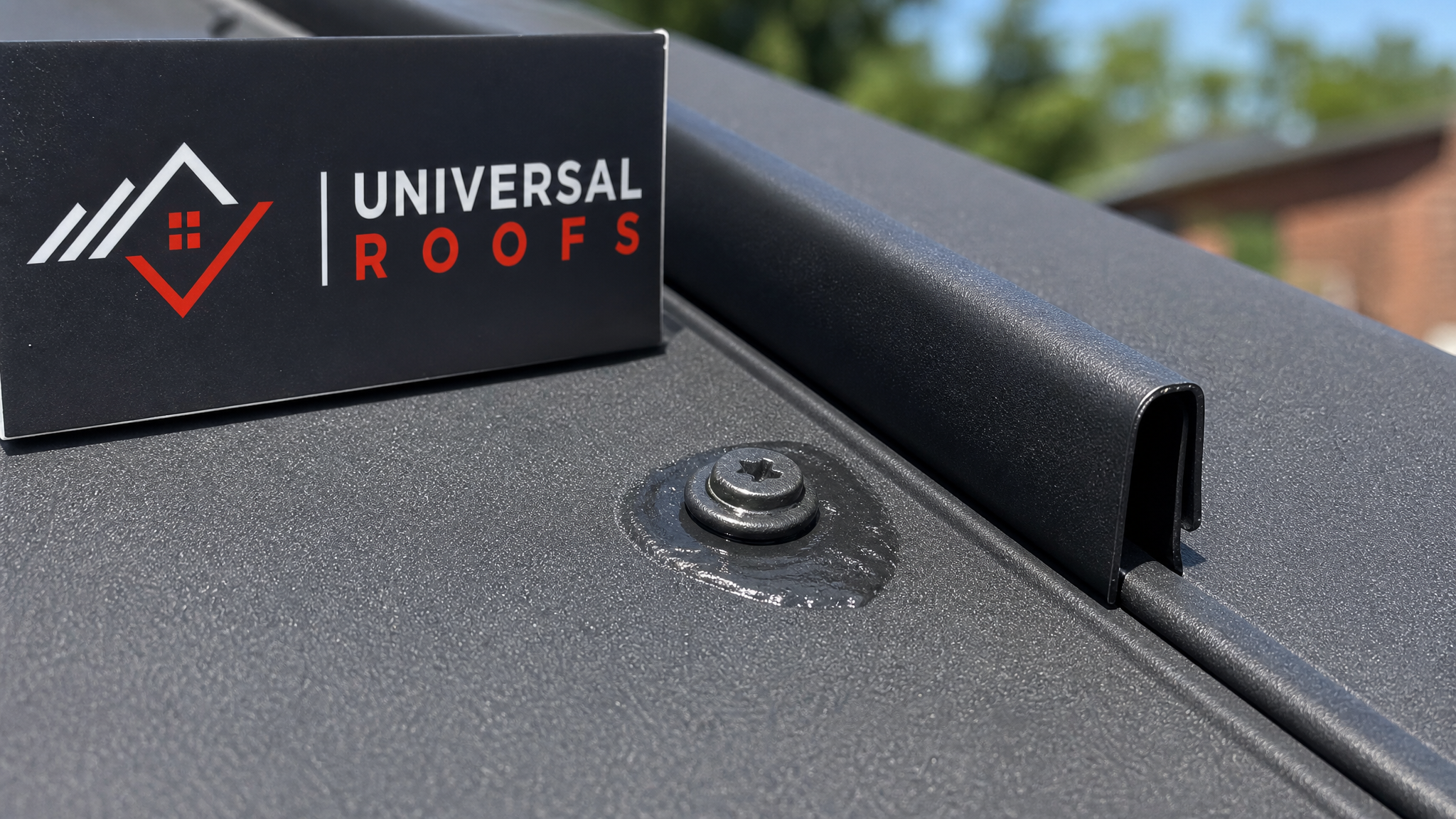 Close-up of a metal roof standing seam and fastener showing sealant repair detail with a Universal Roofs branded sign placard