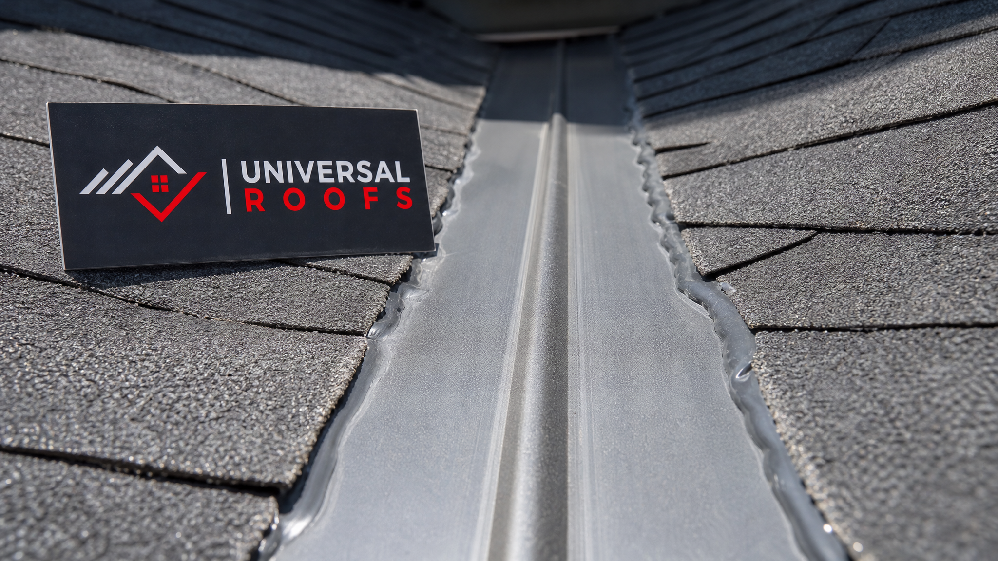 Close-up of new W-profile metal roof valley flashing showing overlapping shingle edges and sealant application
