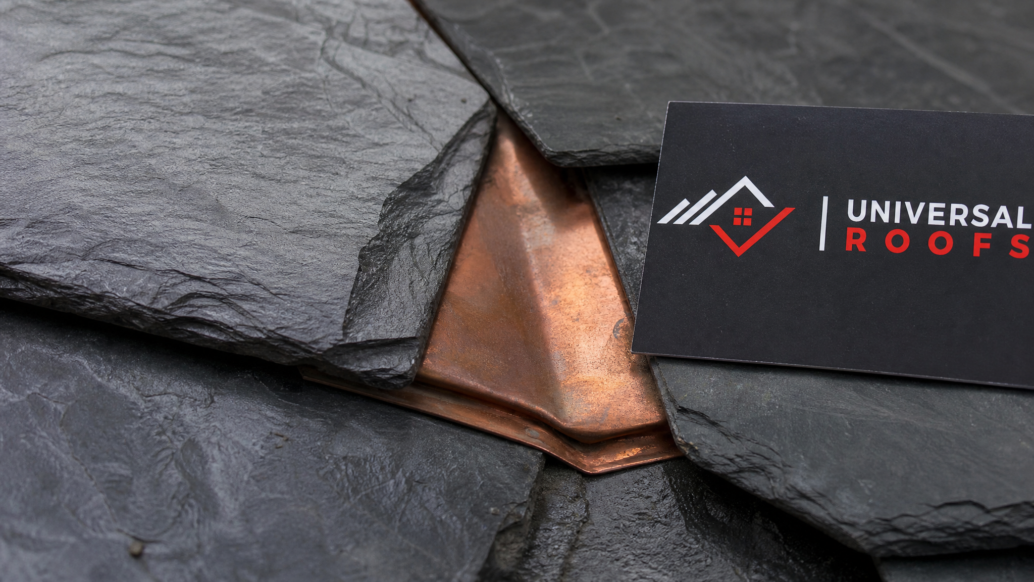 Close-up of hand-repaired heritage slate shingles with copper flashing detail and Universal Roofs sign placard