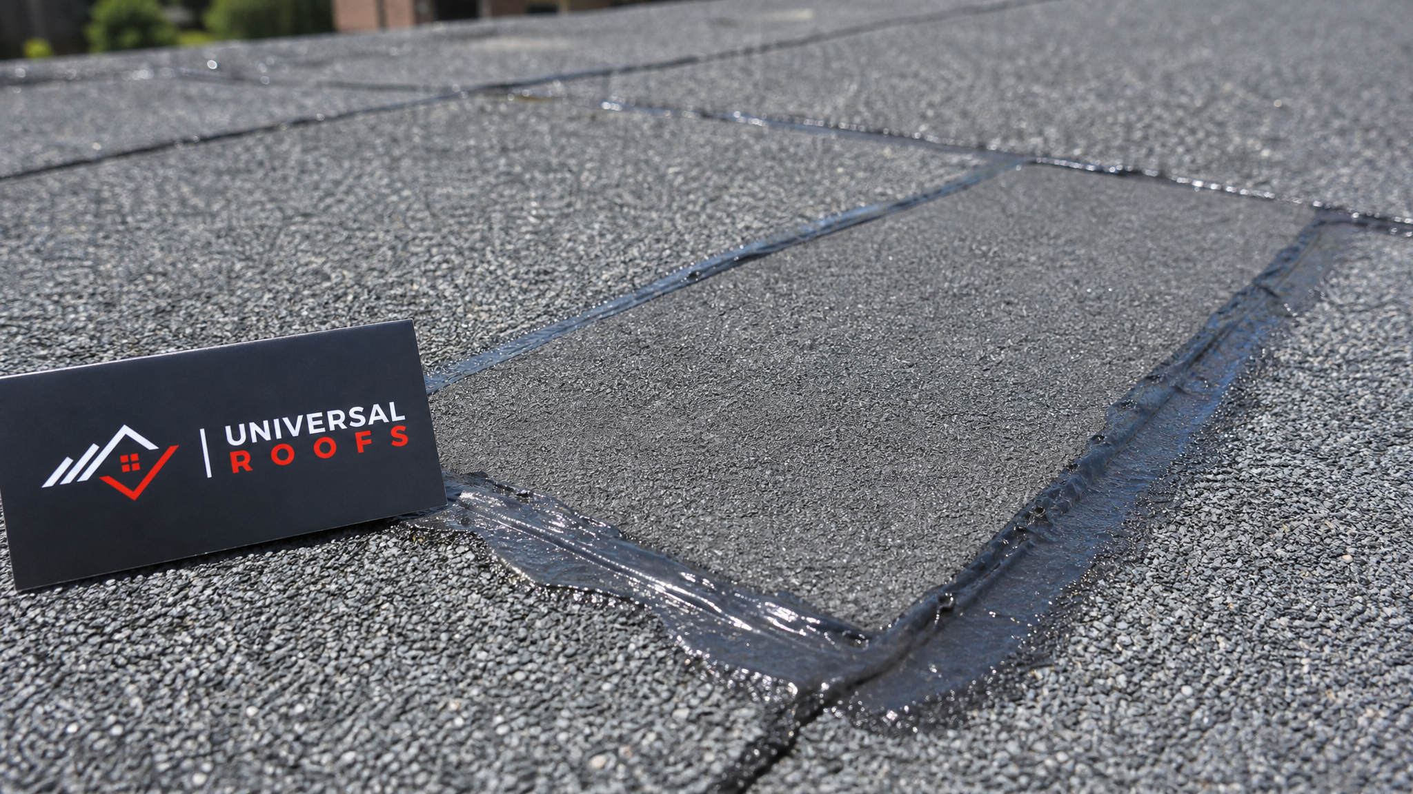 Close-up of a peel-and-stick membrane patch sealed over a flat roof seam with roofing cement, with a Universal Roofs branded sign placard nearby