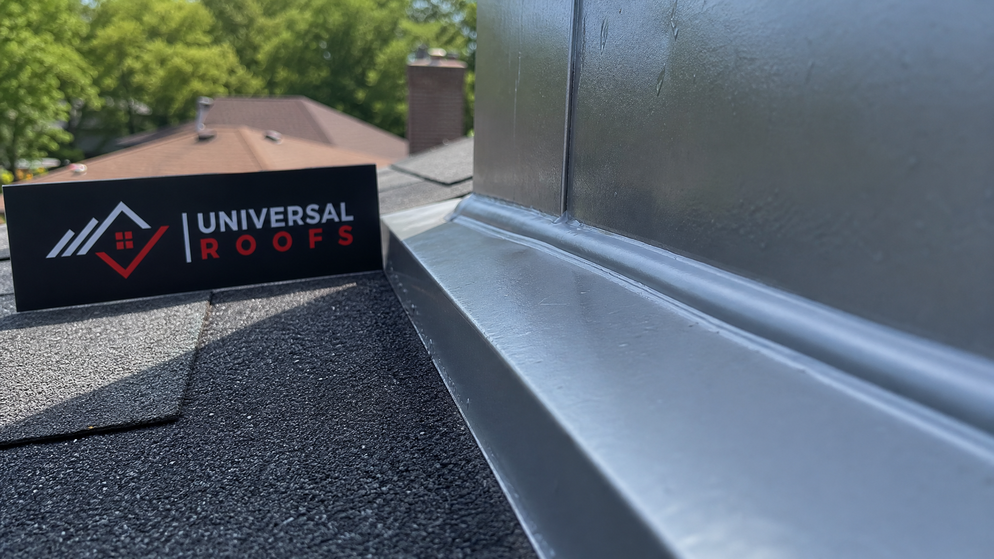 Close-up of freshly applied silicone sealant bead along roof flashing joint with Universal Roofs branded sign nearby