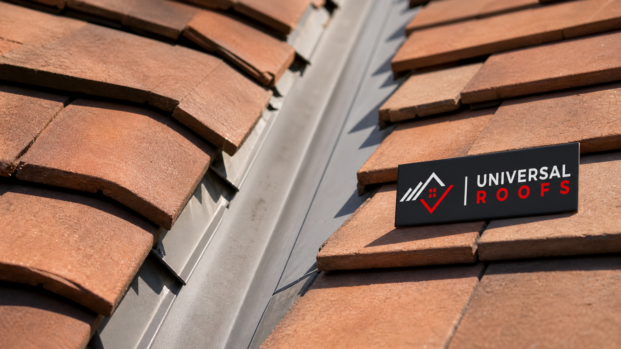 Close-up of overlapping clay roof tiles and metal valley flashing detail with Universal Roofs branded sign placard