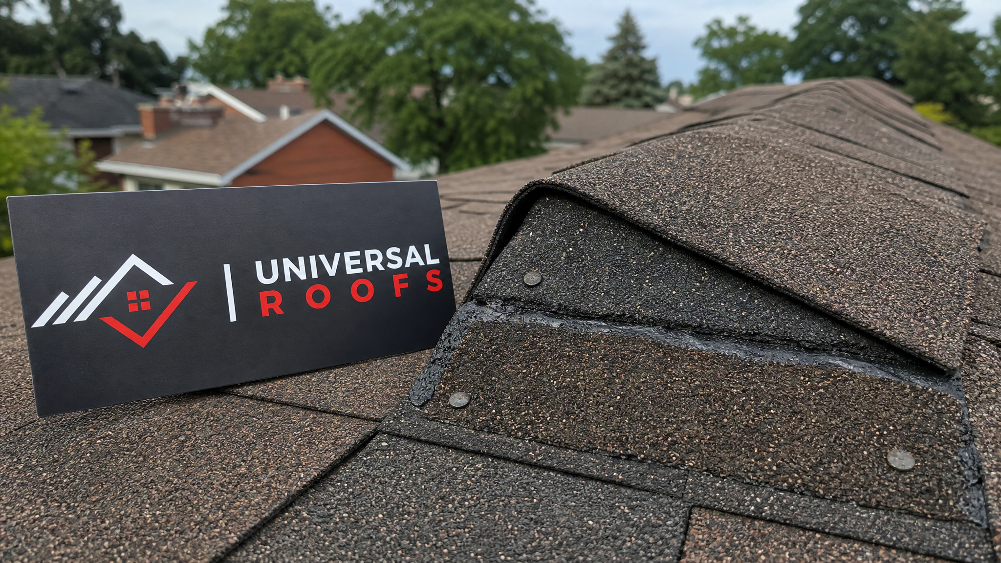 Close-up of new asphalt shingle courses and ridge cap flashing correctly nailed and sealed after wind damage repair