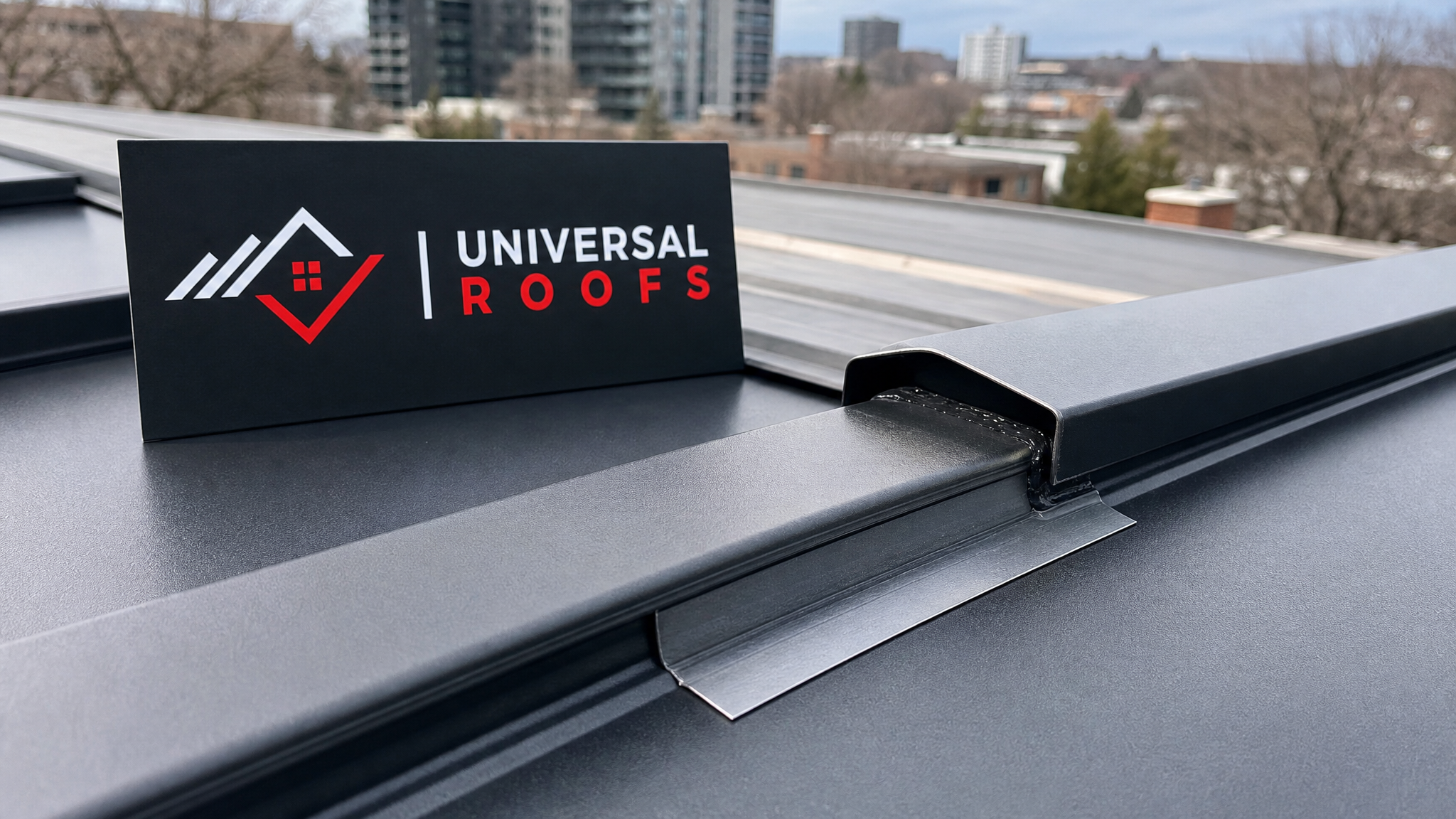 Close-up detail of a repaired standing-seam metal roof joint showing fresh sealant and a matching metal flashing strip, with a Universal Roofs branded sign placard visible nearby