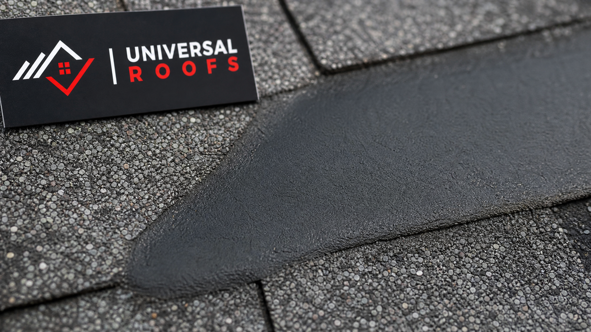 Close-up of a properly feathered rubberized weatherproof roof patch seam with a Universal Roofs branded sign placard nearby