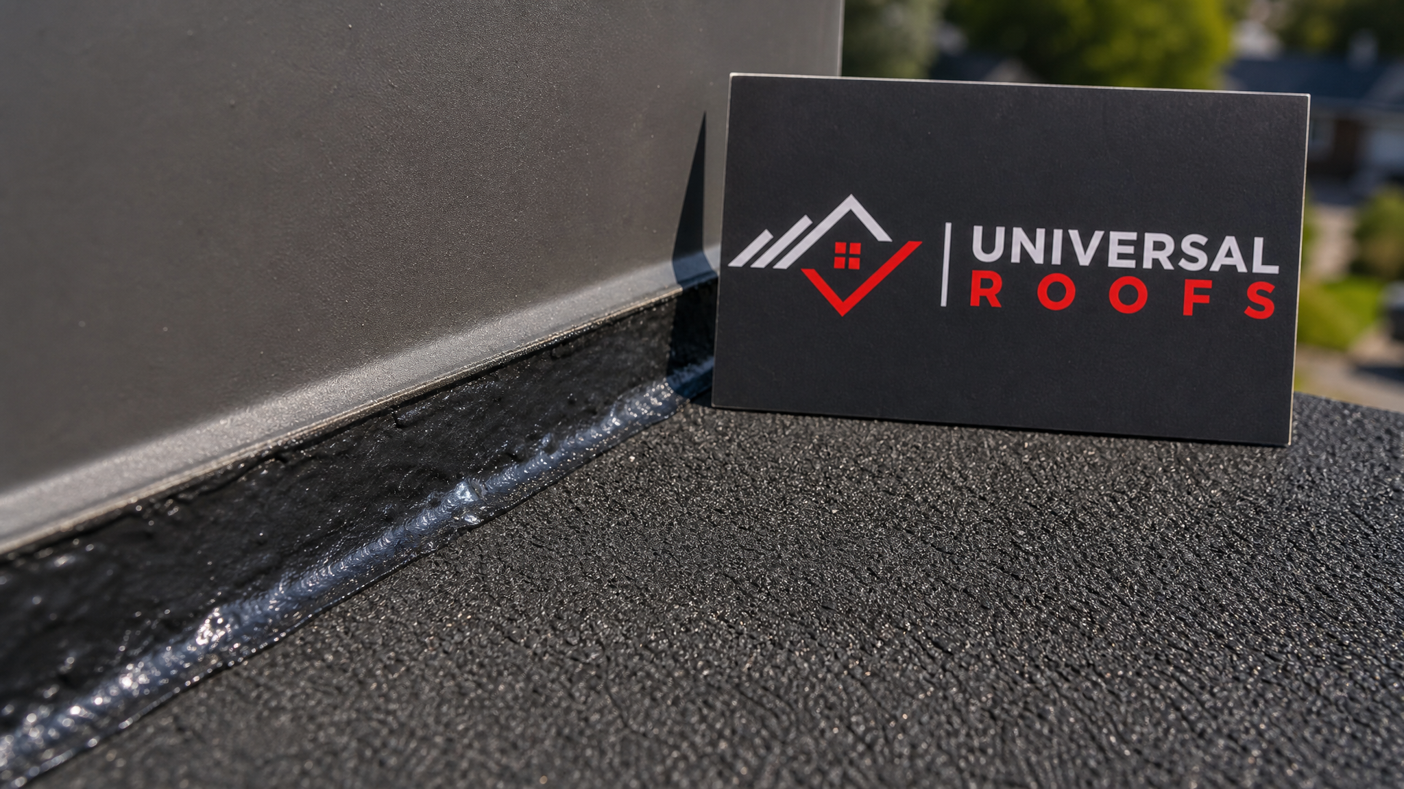 Close-up detail of a modified bitumen roof patch seam sealed against a flashing edge with a Universal Roofs branded sign placard