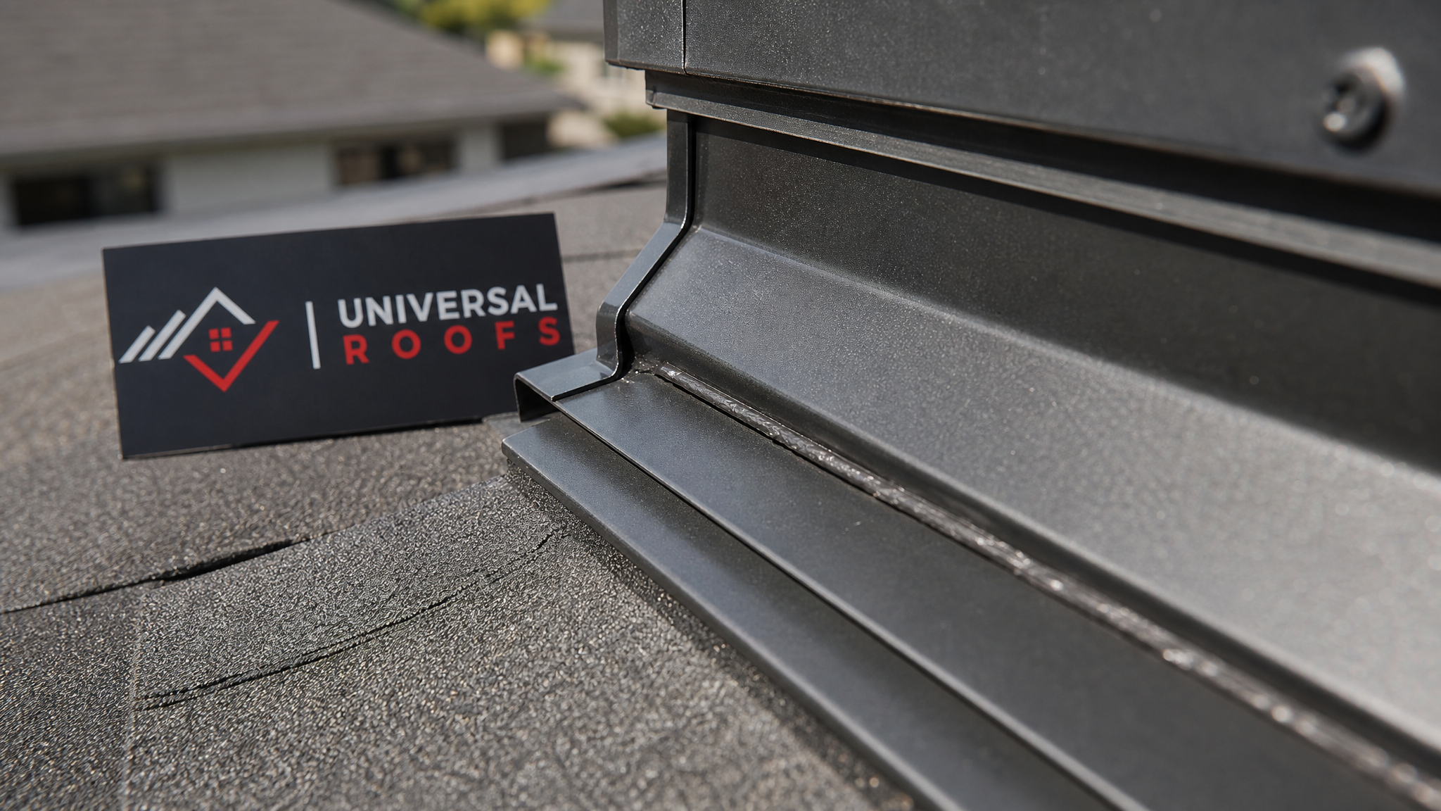 Close-up detail of overlapping counter-flashing and step flashing sealed around an attic access curb with a branded sign placard nearby