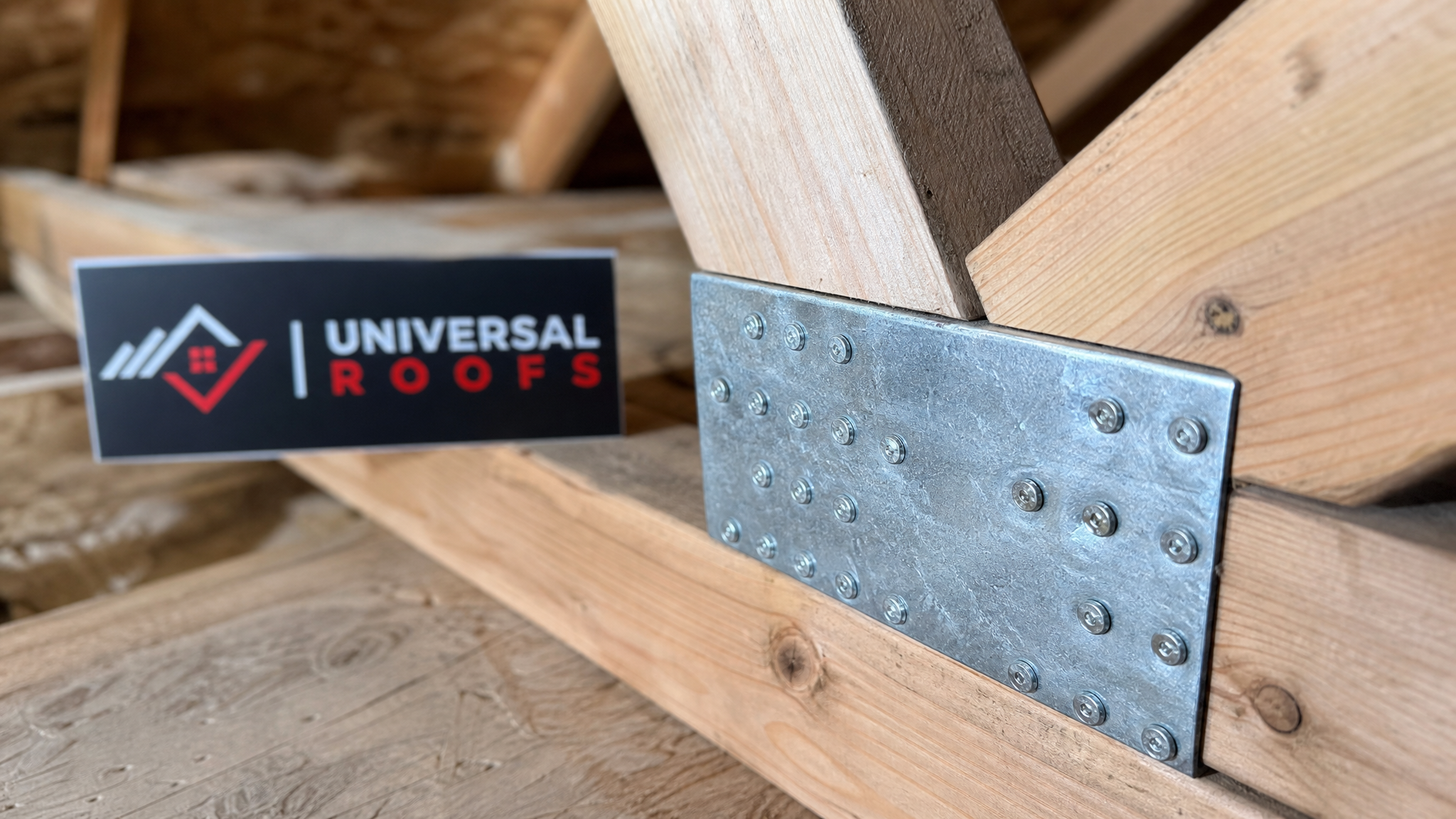 Close-up detail of a repaired truss connector plate and sistered lumber joint in a Toronto attic with a Universal Roofs branded sign placard nearby